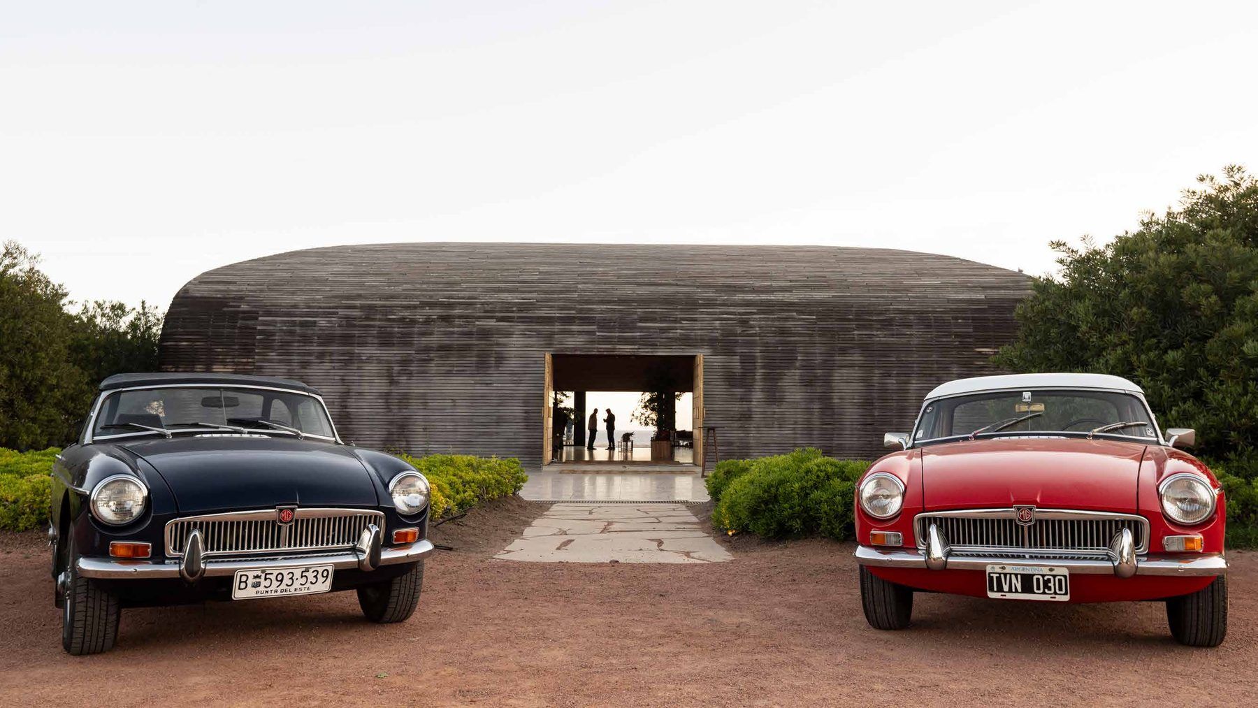 Dos autos MG clásicos frente a un edificio icónico de José Ignacio al atardecer